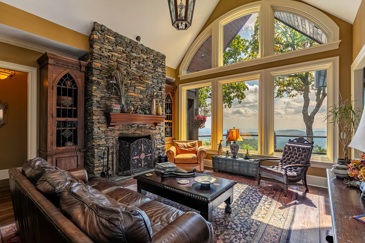 A cozy den featuring a stone fireplace, large windows with scenic views, and plush seating arranged for comfort. The elegant decor and warm ambiance make this space ideal for unwinding, movie nights, or enjoying the company of friends and family.