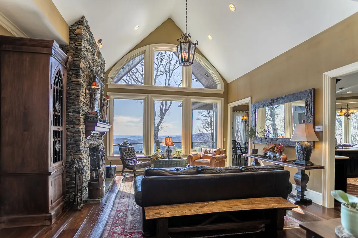A beautifully decorated living area with large windows showcasing a breathtaking sunrise over the mountains, a stone fireplace, comfortable seating, and artistic decor. The room feels intimate yet open, perfectly blending relaxation with inspiration.