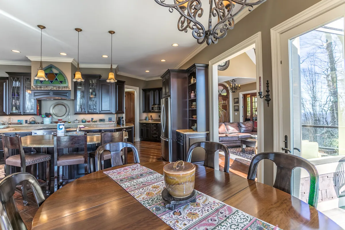 A view of the kitchen island with three bar chairs, elegant cabinetry, and a statement chandelier above the dining table. The layout encourages casual conversations and togetherness, with a clear sightline from the kitchen to the dining area.