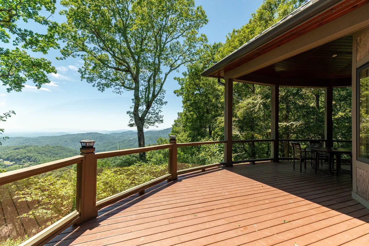 An expansive wooden deck with comfortable outdoor seating, surrounded by lush greenery and offering panoramic views of the mountains. The space suggests a tranquil spot for morning coffee, gatherings, or simply relaxing while immersed in nature.