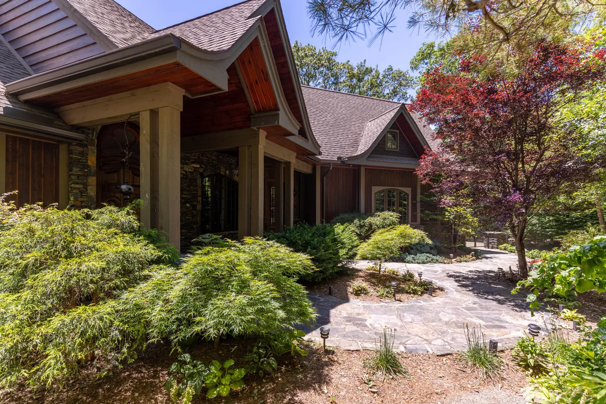 This exterior scene highlights a serene stone pathway winding through lush greenery, with a striking red maple tree and architectural details of the house visible. The scene exudes tranquility and connection to nature, ideal for leisurely strolls or playful moments with pets.