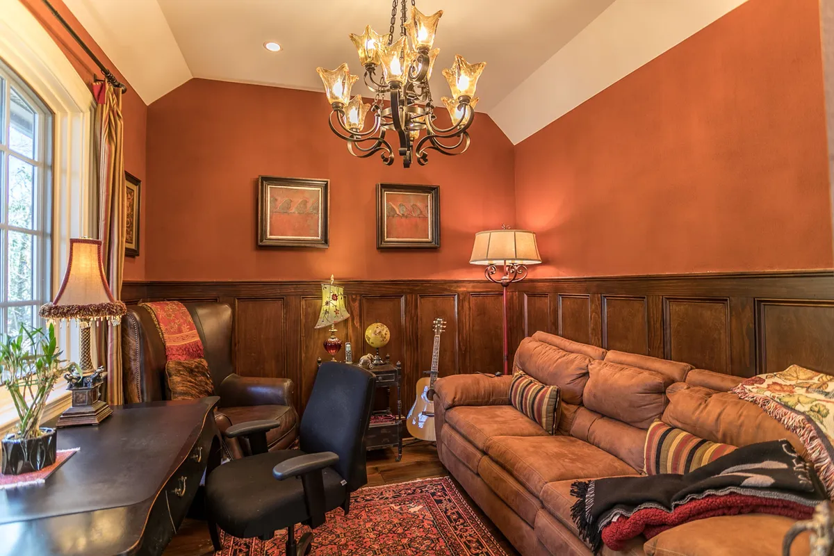 A refined office nook featuring a wooden desk, plush couch, a guitar leaning nearby, elegant chandelier, and tasteful artwork. The setting invites creativity and productivity within a comfortable, sophisticated space.