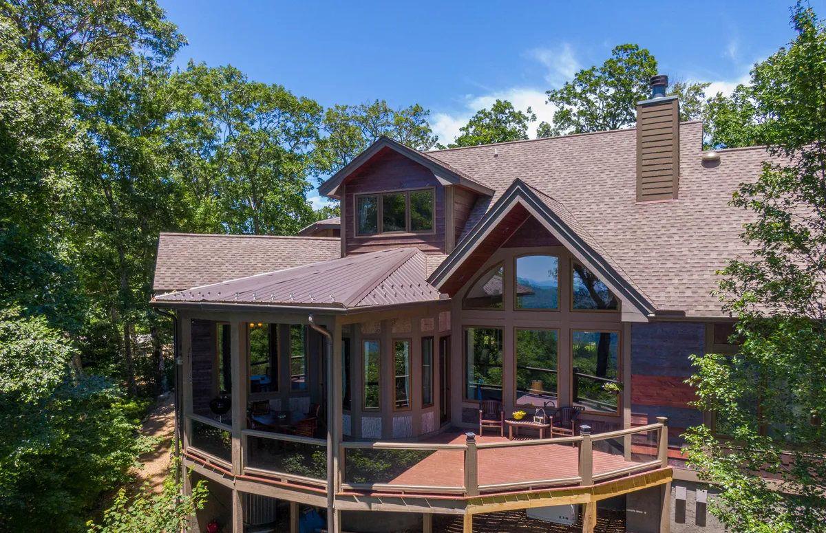 The View House exterior is framed by natural surroundings, including mature trees and a wraparound deck with expansive windows. The tranquil scene hints at both the comfort of the home and its seamless integration with the natural landscape. The deck is perfectly positioned for sunset watching or relaxing after a day of exploration.