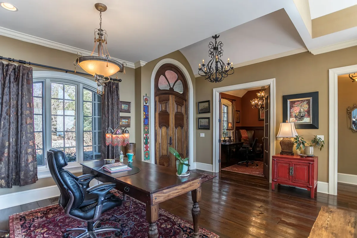A spacious, elegant upstairs office and games lounge with a wooden desk, large windows, chandelier, and artwork. The room offers both productivity and leisure for families and guests.