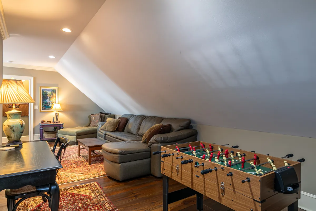 The cozy interior features a foosball table, comfortable sofa, lamp, and wall art, creating a playful and relaxed atmosphere. This space is clearly designed for entertainment and group fun, echoing the foosball, games, and den described in the section.