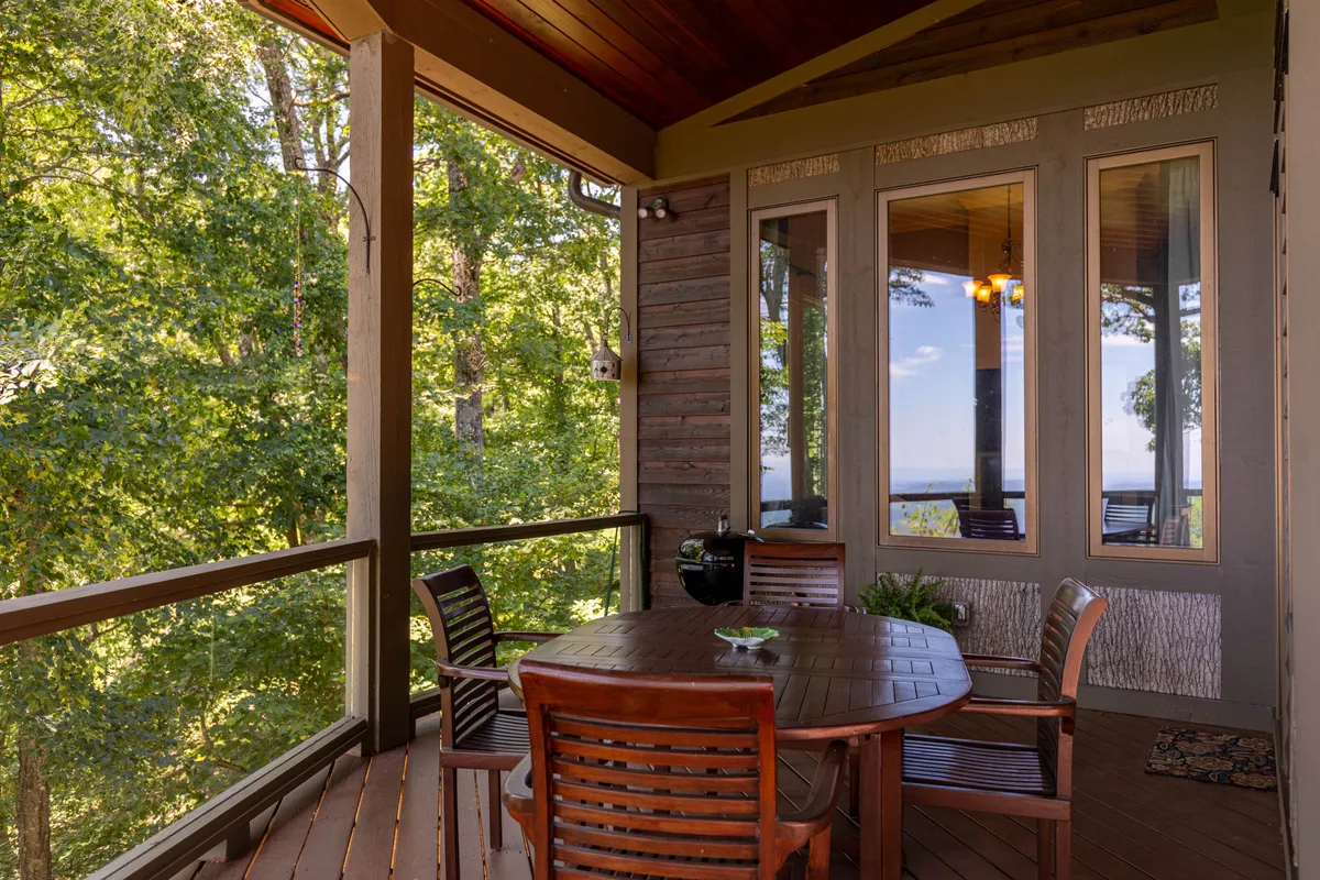 A tranquil outdoor dining area with a wooden table set against a backdrop of lush greenery and large house windows, emphasizing relaxation and a strong connection to the natural surroundings.