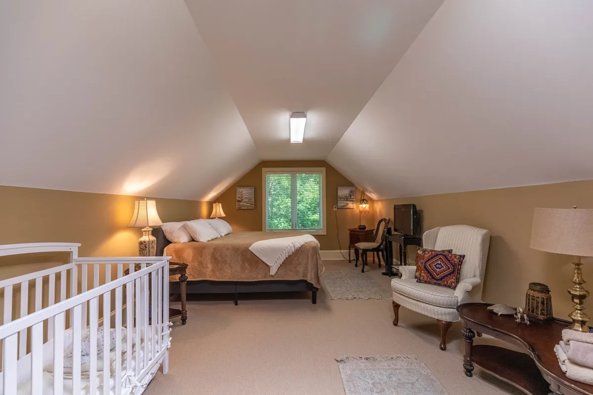 A peaceful bedroom with a bed, crib, window, and armchair, designed for family comfort. The setting invites quiet time, reading, and playful interactions with infants, and includes amenities for little ones.