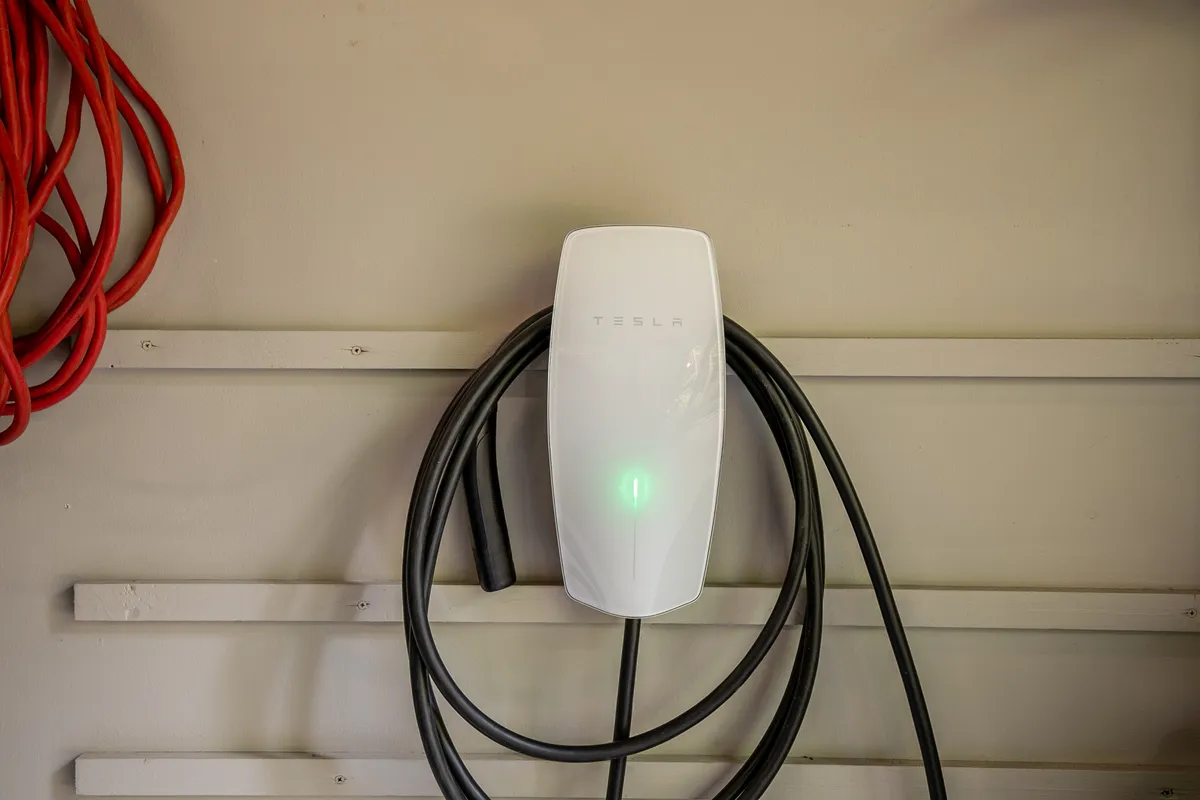 A Tesla wall charger installed in the garage, with red extension cords nearby. The scene highlights the home's electric vehicle charging capability, underlining its modern amenities and appeal for eco-conscious guests.
